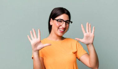 Gülümsüyor ve dost canlısı görünüyor, onuncu ya da onuncu numarayı gösteriyor, eli önde, geri sayıyor.