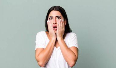 Şok olmuş ve korkmuş hissediyorum, ağzı açık ve elleri yanaklarında korkmuş görünüyor.