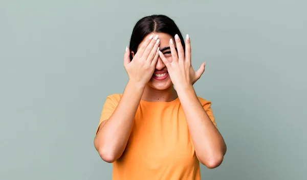 covering face with hands, peeking between fingers with surprised expression and looking to the side