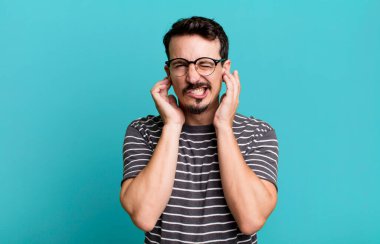 Kızgın, stresli ve sinirli görünüyor, iki kulağı da sağır edici bir ses, ses ya da yüksek sesle kapatıyor.