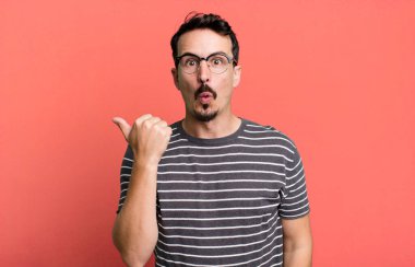 İnançsızlıktan şaşkın şaşkın bakıyor, yan taraftaki objeyi işaret ediyor ve 