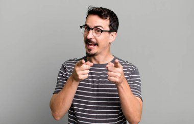 Pozitif, başarılı, mutlu bir tavırla kamerayı işaret ederek, elleriyle silah işareti yaparak.