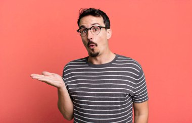 Şaşırmış ve şoke olmuş bir halde, çenesi düşmüş bir objeyi elinde açık bir elle tutarken.