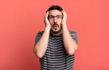 Kötü bir şekilde şoke olmuş, korkmuş ya da endişeli, ağzı sonuna kadar açık ve iki kulağını da eliyle kapatmış.