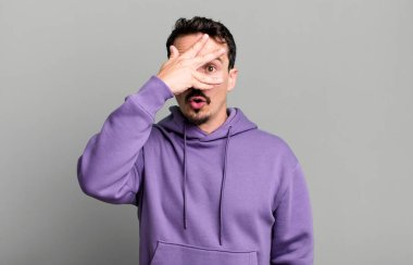 Şok olmuş, korkmuş ya da korkmuş görünüyor, yüzleri elle kaplıyor ve parmaklarının arasına bakıyor.