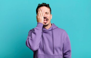 Uykulu görünüyor, sıkılmış ve esniyor, baş ağrısı ve yüzünün yarısını kaplayan bir elle.