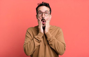 Şok olmuş ve korkmuş hissediyorum, ağzı açık ve elleri yanaklarında korkmuş görünüyor.