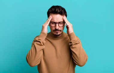 Stresli ve hayal kırıklığına uğramış görünüyor, baskı altında çalışıyor, baş ağrısı ve sorunlarla boğuşuyor.