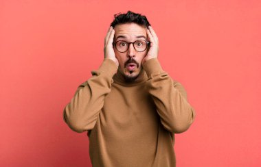 Kötü bir şekilde şoke olmuş, korkmuş ya da endişeli, ağzı sonuna kadar açık ve iki kulağını da eliyle kapatmış.