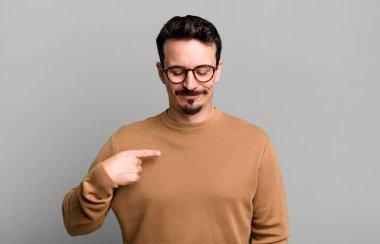 Neşeli bir şekilde gülümsüyor, aşağıya bakıyor ve göğsünü işaret ediyor.