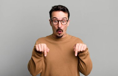Şok olmuş, ağzı açık ve şaşkın, inançsızlık ve şaşkınlık içinde bakıyor ve aşağı doğru işaret ediyor.