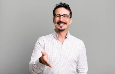 Gülümsüyor, mutlu görünüyor, kendinden emin ve arkadaş canlısı, anlaşmayı bitirmek için el sıkışmayı teklif ediyor, işbirliği yapıyor.