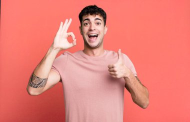 Adam mutlu, şaşkın, tatmin olmuş ve şaşırmış hissediyor, tamam gösteriyor ve el kol hareketi yapıyor, gülümsüyor.