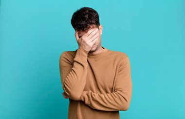 Stresli, utanmış ya da üzgün görünen bir adam. Başı ağrıyordu. Yüzü elle kaplıydı.