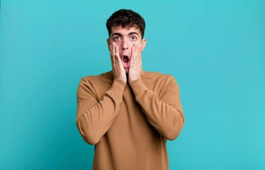 Adam şok olmuş ve korkmuş hissediyor, ağzı açık ve elleri yanaklarında korkmuş görünüyor.