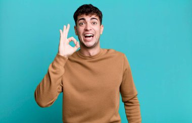 Adam kendini başarılı ve tatmin olmuş hissediyor, ağzı açık gülümsüyor, elle işaret veriyor.