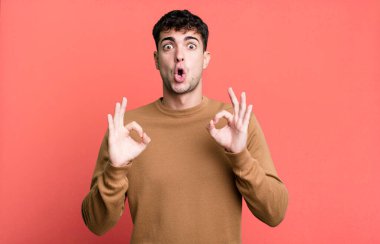 Şok olmuş, şaşırmış ve şaşırmış hisseden bir adam, iki eliyle onay işareti yapıyor.