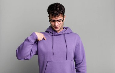 Adam neşeyle gülümsüyor, yere bakıyor ve göğsünü işaret ediyor.