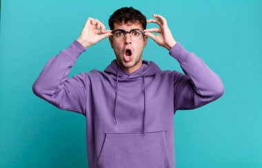 Şok olmuş, şaşırmış ve şaşırmış hisseden bir adam, elinde şaşkın, inançsız bir bakışla gözlük tutuyor.