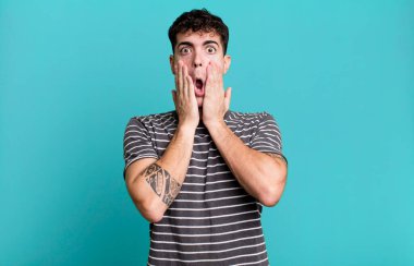 Şok olmuş ve korkmuş hissediyorum, ağzı açık ve elleri yanaklarında korkmuş görünüyor.