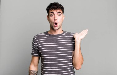 Şaşırmış ve şoke olmuş bir halde, çenesi düşmüş bir objeyi elinde açık bir elle tutarken.