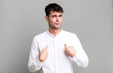 Kafası karışık ve tuhaf bakışlarla kendini işaret eden bir adam, seçildiğine şaşırmış ve şaşırmış.