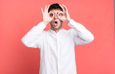 Şok olmuş, şaşırmış ve şaşırmış hisseden bir adam, elinde şaşkın, inançsız bir bakışla gözlük tutuyor.