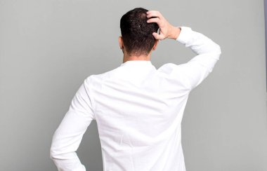 Kendini cahil ve kafası karışık hisseden bir adam, bir çözüm düşünüyor, eli kalçasında, diğeri kafasında, dikiz aynasından.