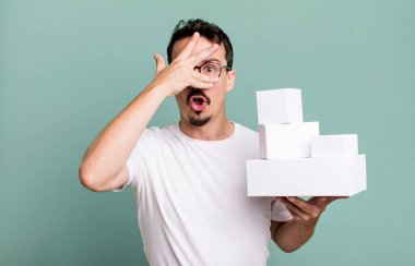 adult man looking shocked, scared or terrified, covering face with hand. blank boxes packaging concept
