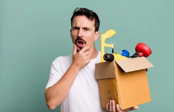 adult man with mouth and eyes wide open and hand on chin. with a toolbox. handyman concept