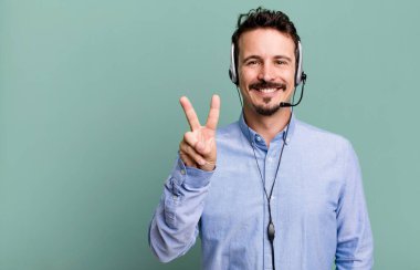 Yetişkin bir adam gülümsüyor ve arkadaş canlısı görünüyor. İki numarayı kulaklıkla gösteriyor. tele pazarlamacı konsepti