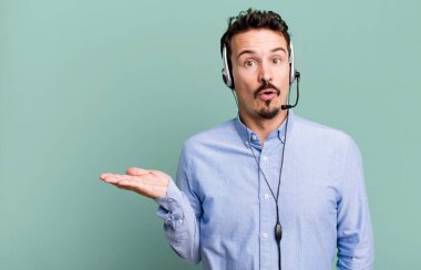 Yetişkin bir adam şaşırmış ve şok olmuş görünüyor. Çenesi düşmüş ve elinde kulaklıkla bir nesne tutuyor. tele pazarlamacı konsepti