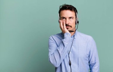 Yetişkin bir adam, kulaklık taktıktan sonra sıkılmış, hayal kırıklığına uğramış ve uykulu hissediyor. tele pazarlamacı konsepti