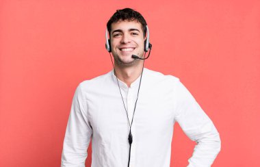 Yetişkin bir adam mutlu bir şekilde gülümsüyor, eli kalçasında ve kulaklığı var. tele pazarlamacı konsepti