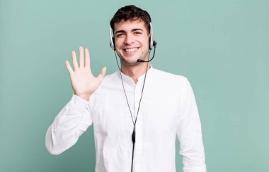 Yetişkin bir adam mutlu bir şekilde gülümsüyor, el sallıyor, sizi selamlıyor ve kulaklıkla selamlıyor. tele pazarlamacı konsepti