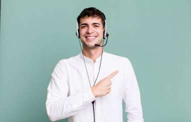 Yetişkin bir adam neşeyle gülümsüyor, mutlu hissediyor ve kulaklıkla bir tarafı işaret ediyor. tele pazarlamacı konsepti