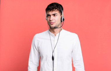 Yetişkin bir adam üzgün, üzgün ya da kızgın ve kulaklıkla yan tarafa bakıyor. tele pazarlamacı konsepti