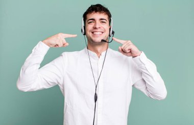 Yetişkin bir adam kendine güvenerek kulaklıkla kendi geniş gülüşünü işaret ediyor. tele pazarlamacı konsepti