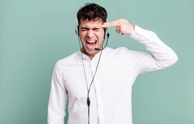 Yetişkin bir adam mutsuz ve stresli görünüyor, intihar jesti kulaklıkla silah işareti yapıyor. tele pazarlamacı konsepti