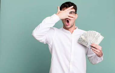 Yetişkin bir adam şok olmuş, korkmuş ya da korkmuş görünüyor, yüzünü elle kapatıyor. Dolar banknotları konsepti