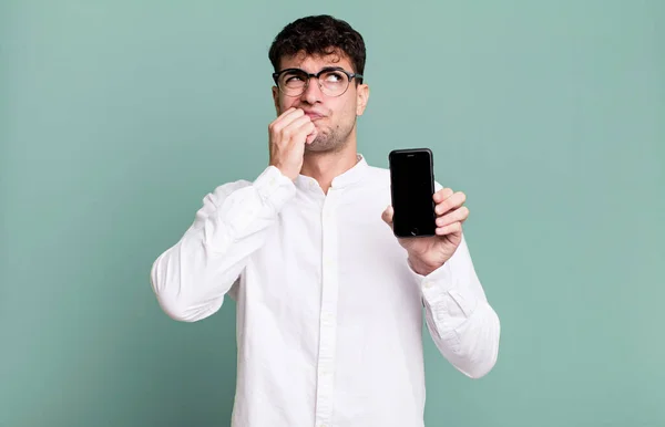 adult man thinking, feeling doubtful and confused and showing his smartphone screen