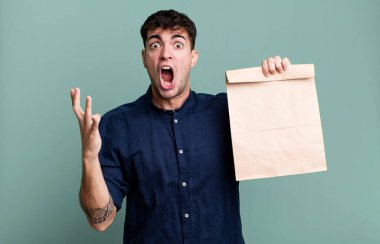 Yetişkin bir adam kahvaltı poşeti ve paket kâğıdıyla bir paket kahvaltıya şaşırır ve şok olur.