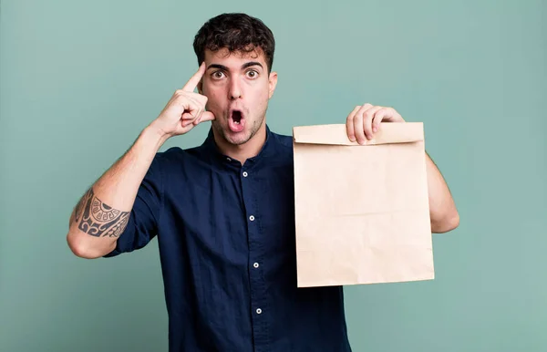adult man looking surprised, realizing a new thought, idea or concept with a take away breakfast paper bag with a take away breakfast paper bag