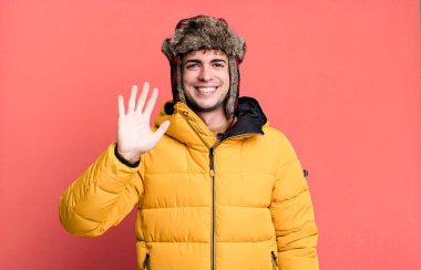 Yetişkin bir adam mutlu bir şekilde gülümser, el sallar, seni karşılar ve anorak giyerek selamlar. kış ve soğuk konsept