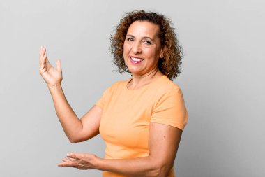 Orta yaşlı İspanyol kadın gururla ve kendinden emin bir şekilde gülümsüyor, mutlu ve tatmin olmuş hissediyor ve fotokopi alanında bir konsept gösteriyor.