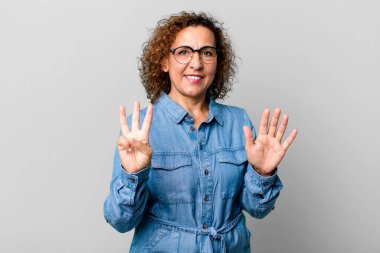 Orta yaşlı İspanyol kadın gülümsüyor ve arkadaş canlısı görünüyor, 8 ya da 8 numarayı gösteriyor, elleri önde, geri sayıyor.