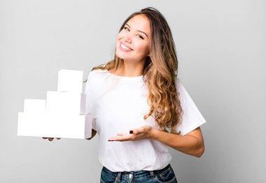 İspanyol güzel kadın neşeyle gülümsüyor, mutlu hissediyor ve beyaz kutular ile bir konsept gösteriyor.