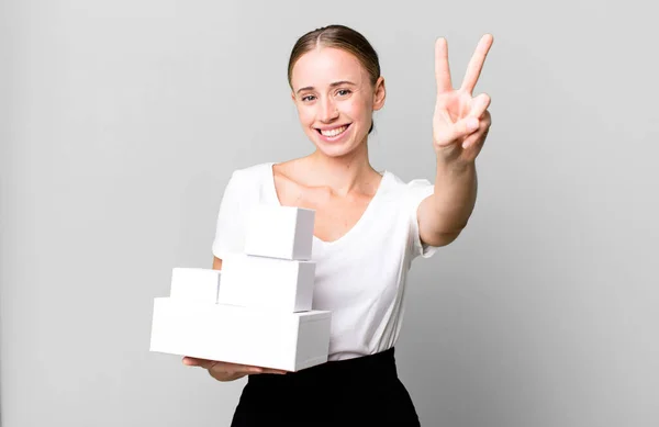 白人女性は笑顔で幸せそうに見える勝利や平和を白い箱のパッケージでジェスチャー — ストック写真