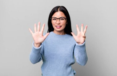 Güzel Latin bir kadın gülümsüyor ve arkadaş canlısı görünüyor. 9 ya da 9 numarayı gösteriyor. Eli önde, geriye doğru sayıyor.