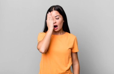 Güzel Latin bir kadın uykulu görünüyor, sıkılmış ve esniyor, baş ağrısı ve yüzünün yarısını kaplayan bir eliyle